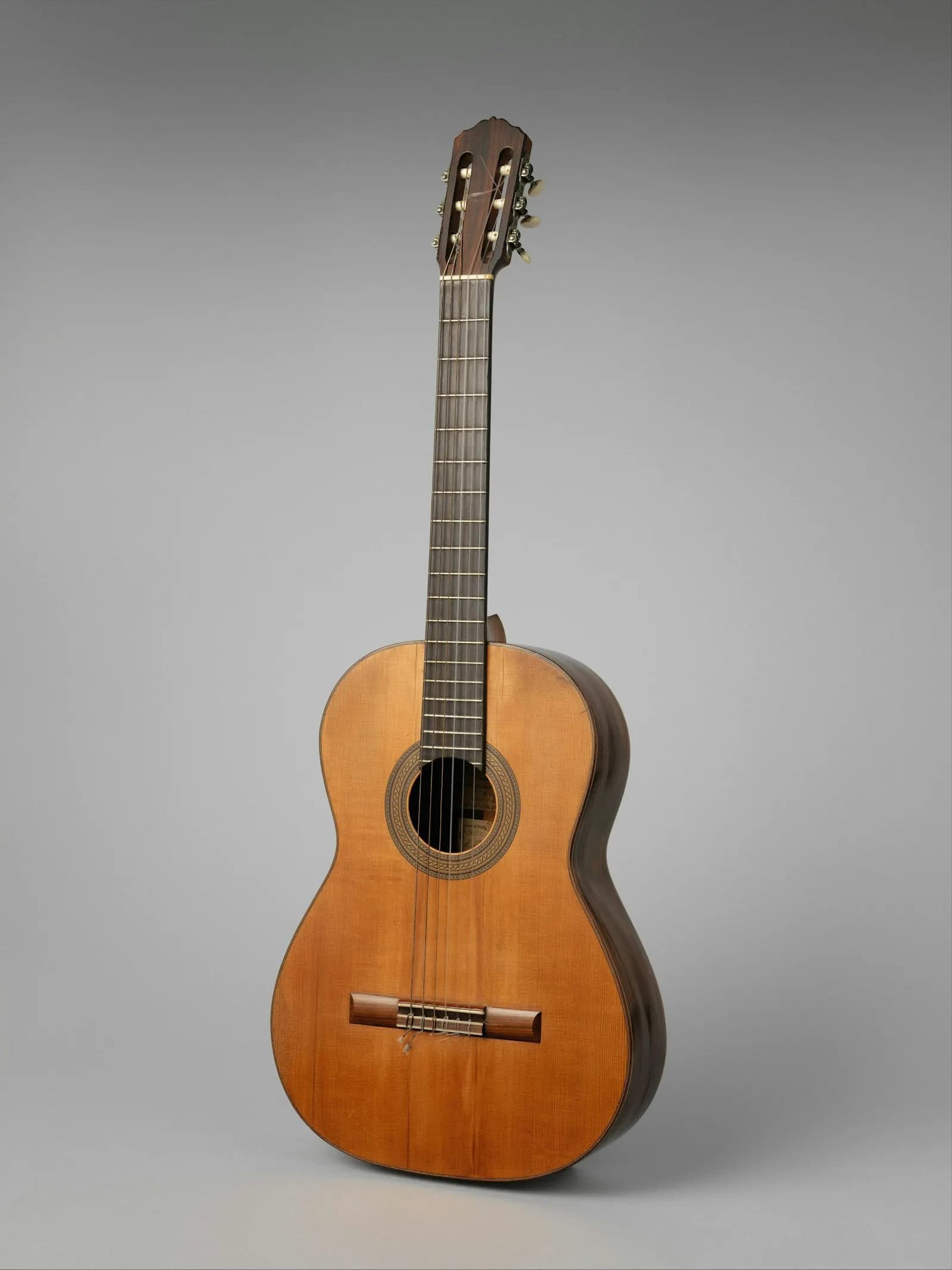 A classical guitar standing upright against a grey backdrop