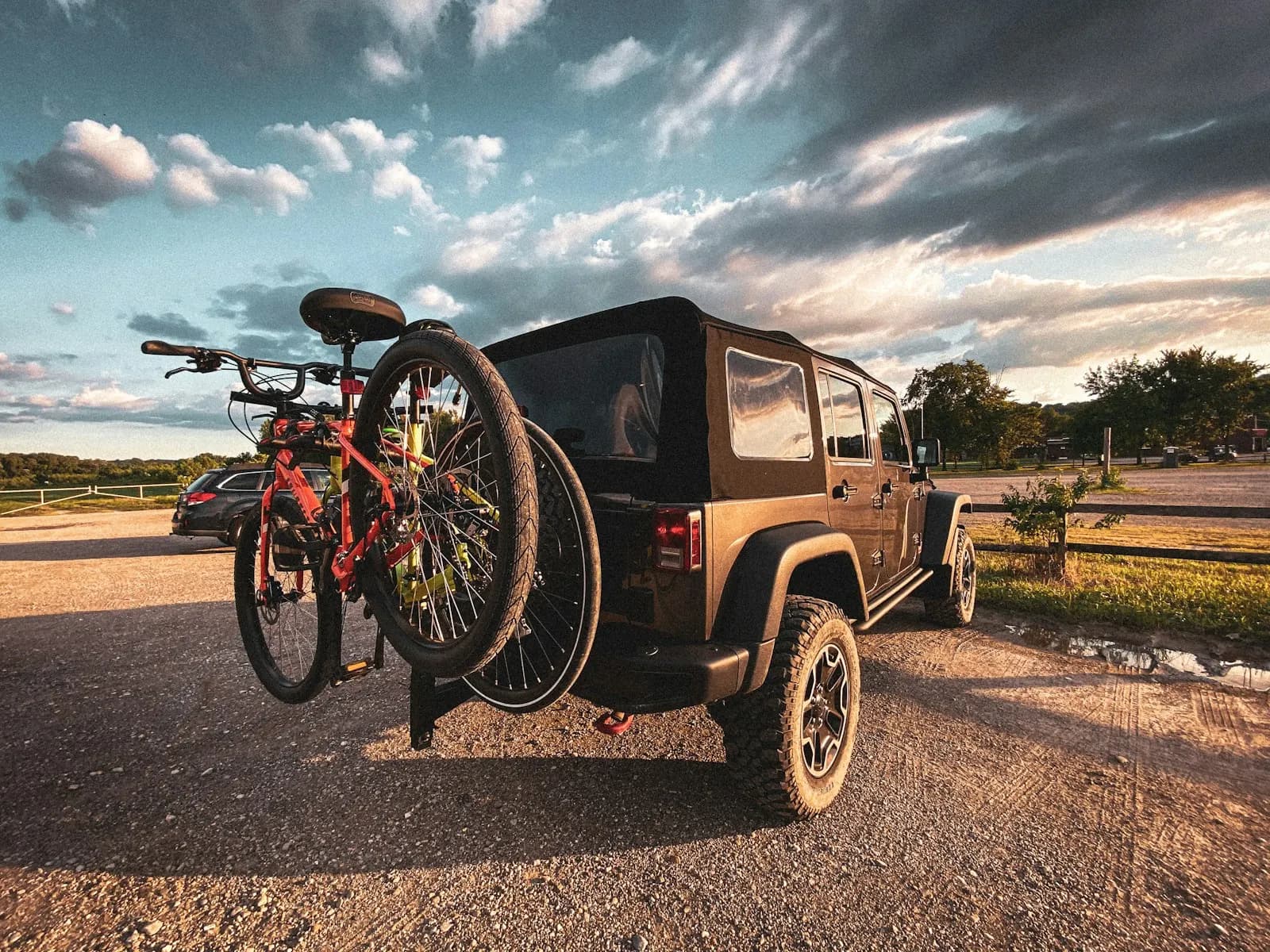 Two bikes on a hitch rack on the back of an SUV, parked on a gravel lot at sunset