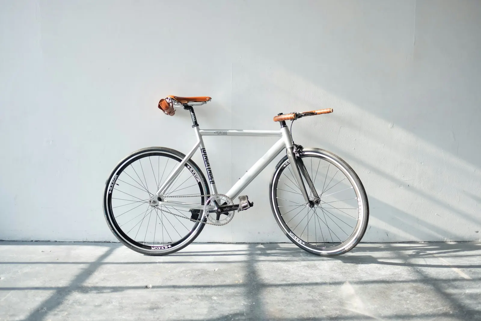 A white city bike with a tan saddle against a bright wall