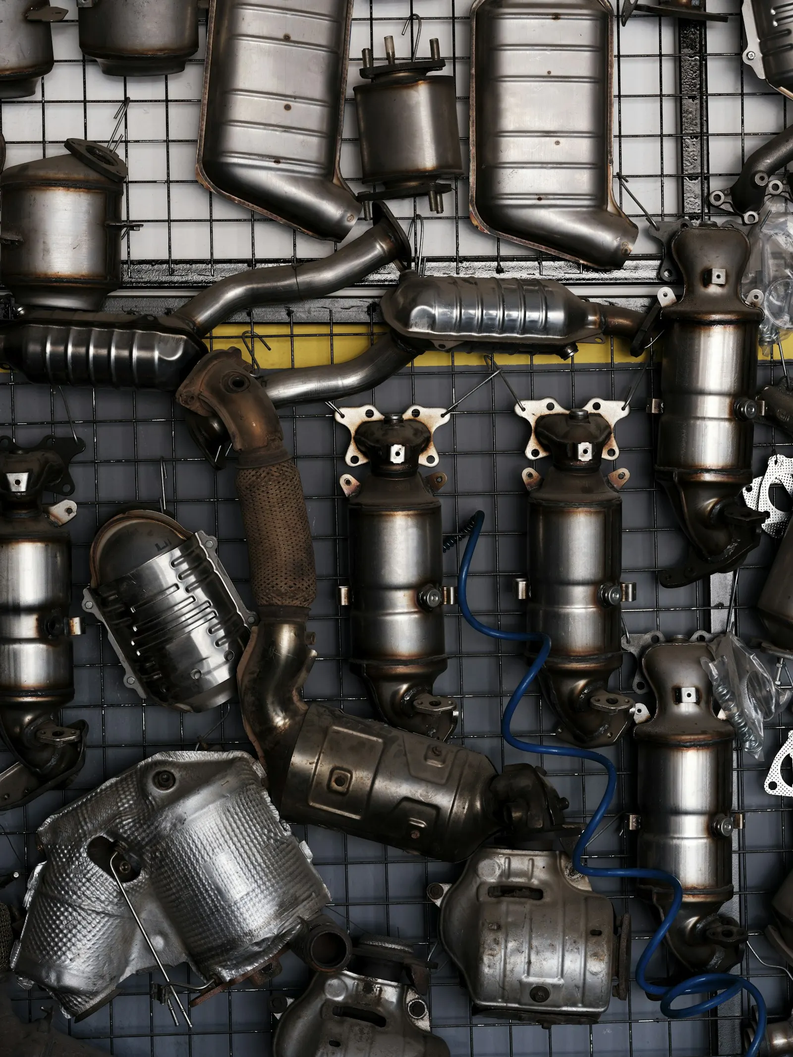 Exhaust pipes and catalytic converters hung on a wall grid