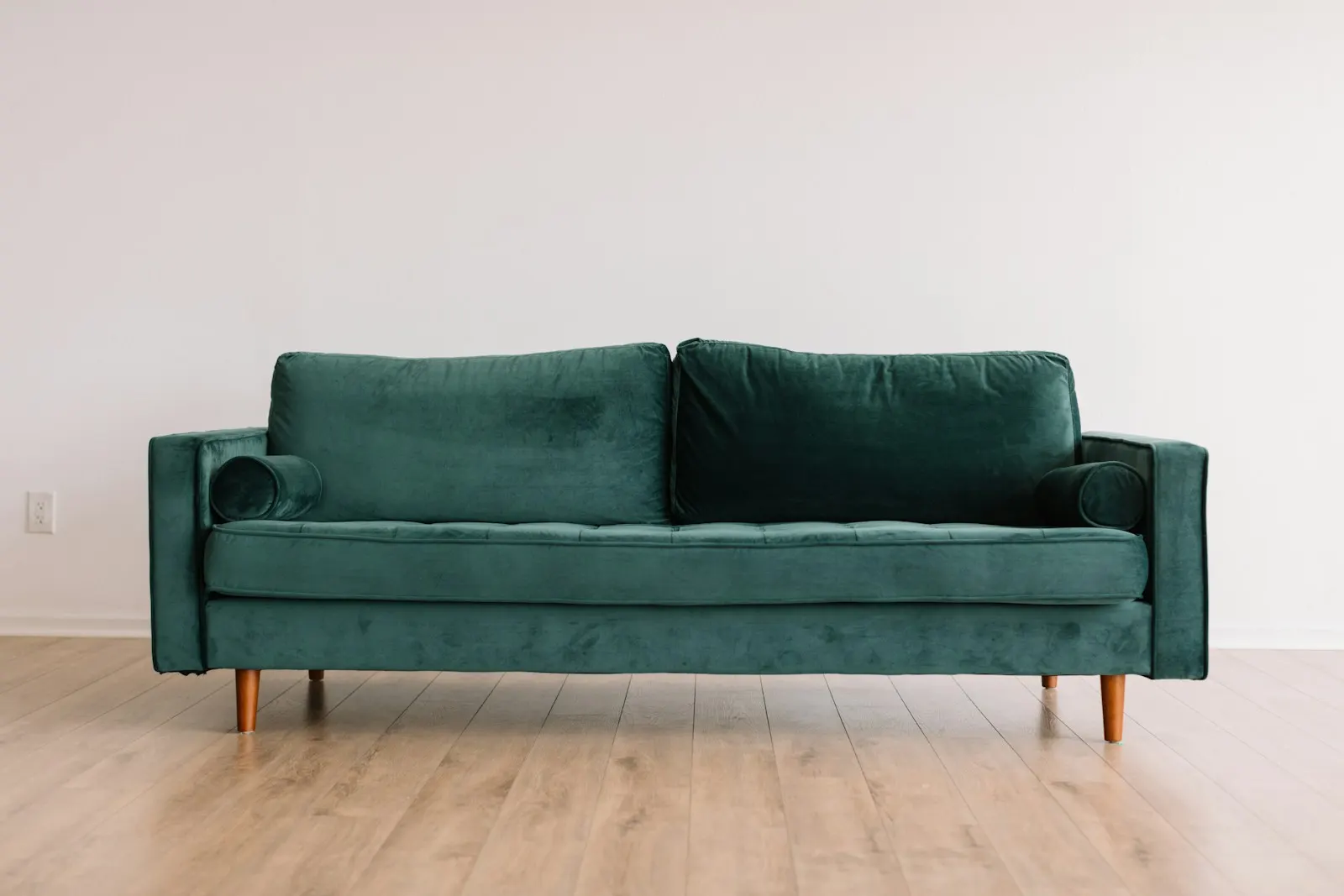 A green velvet sofa on wooden legs in an empty room