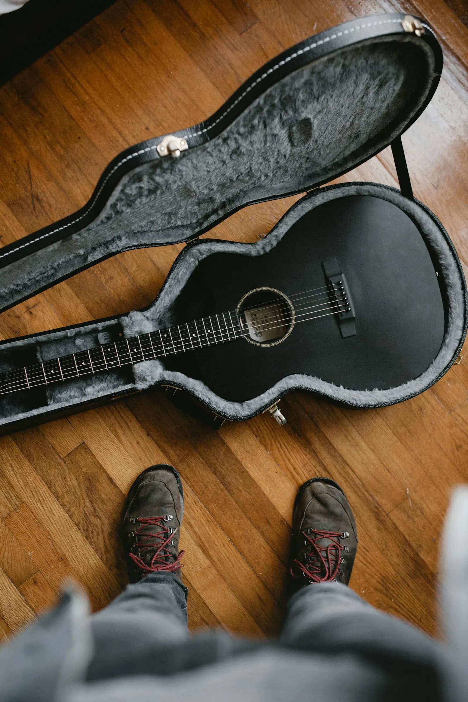 An acoustic guitar lying in an open hard case on a wooden floor
